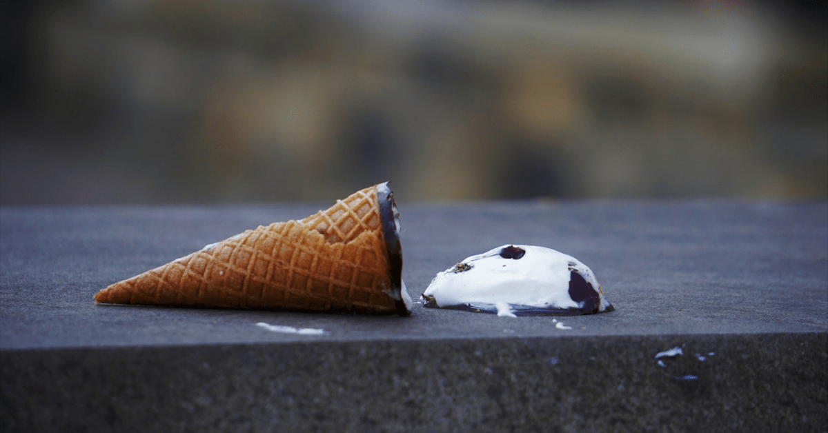 A cone with a scoop of ice cream next to it, which has fallen out onto the surface.